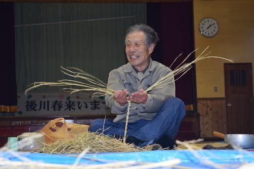 座ってばらばらの稲わらからきれいな編み込みを作っていく講師の今西さんの写真