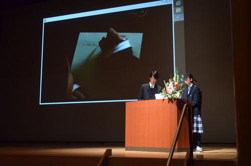 多目的ホール壇上スクリーンを使って発表する東雲高校の生徒男女二人の写真