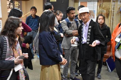 丹波杜氏記念館で丹波杜氏組合の男性から日本酒の作り方と文化についての説明を熱心に聞いている参加者らの様子の写真