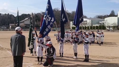 晴天のグラウンドに並び、紺色の応援団旗を掲げて選手宣誓する球児達の写真