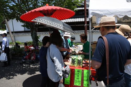 赤い和傘が目を引くブースで来場者に新茶を販売する様子の写真