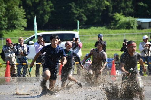 田んぼの中の泥をはね上げながら全力疾走するリレー参加者の皆さんの写真