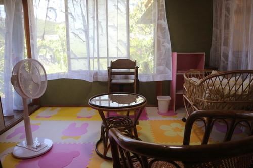 椅子と扇風機と赤ちゃんベットが用意された一室の写真