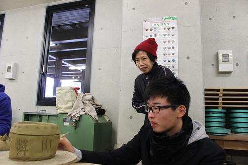 出来上がった陶器に模様を入れる補助をする東雲高校生の男子学生と体験者の方の写真
