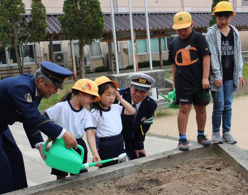 代表の子どもたちが篠山署員とともに校庭の花壇に種を植え、丁寧に土と水をかけて成長を祈っている写真