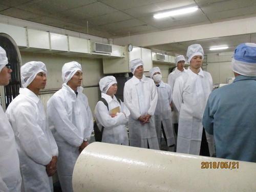 黄桜株式会社にて白い作業着と帽子を着て説明を受ける教職員の皆さんの写真