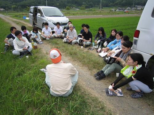 農作業体験の参加者がぐるりと輪になって座って話を聞いている写真