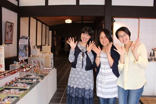 つやつやみおさん、宮崎恵巳さん、岸田万穂さんが鳳凰会館の展示販売品の前で笑顔で並んでポーズをとっている写真