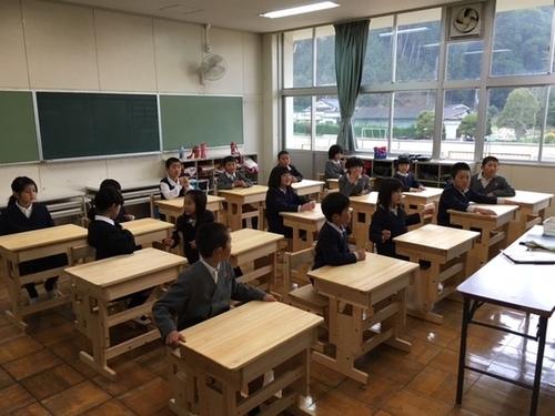 教室に導入された新しいヒノキの机と椅子に座り、嬉しそうな児童たちの写真