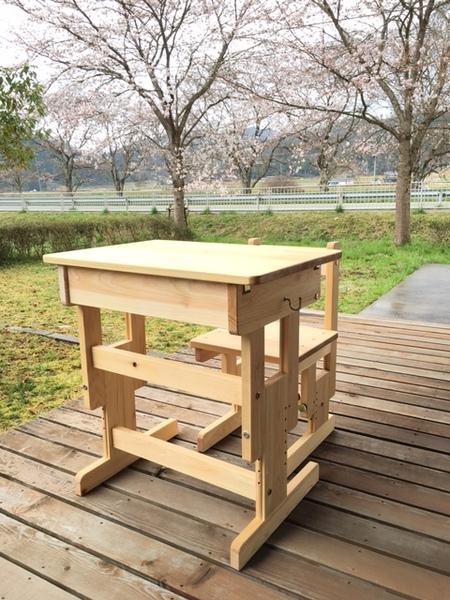 桜の木が見えるウッドデッキに置かれたヒノキの机と椅子の写真