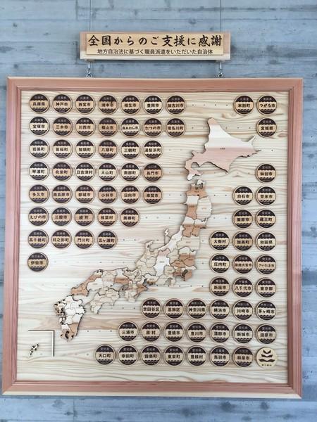 日本地図の周りに自治体名が書かれた丸いプレートを配置した木製の四角いプレートの写真