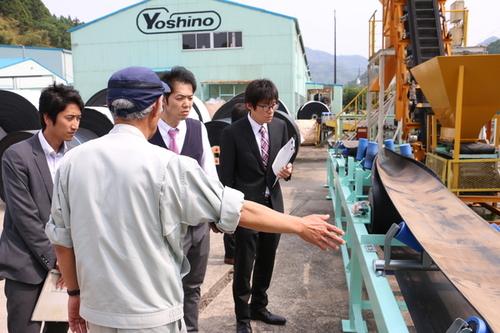 吉野ゴム工業株式会社にて屋外の機械の説明を受ける教職員の皆さんと説明する職員の写真