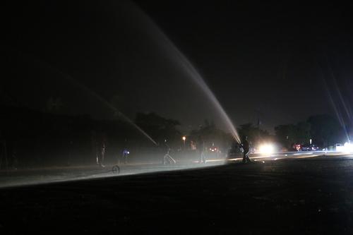 暗闇の中でホースを持った隊員が並び、空に向かって勢いよく放水している写真