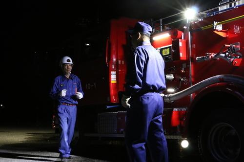 消防車の脇で照らされるライトの光に照らされて向かい合う2名の消防団員の方の写真