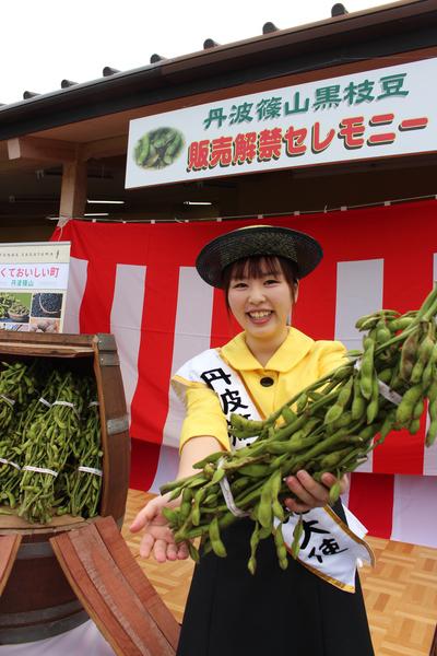 丹波篠山黒枝豆販売解禁セレモニーの会場で黒枝豆をもつ丹波篠山観光大使の女性の写真