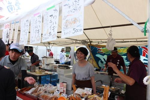 じゃこ天やカワハギの揚げ物が並ぶ愛媛県愛南町からの出店で、商品の説明をしている男性と笑顔で対応する女性の写真