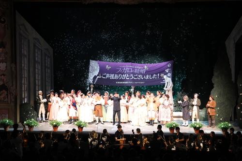中央にフィガロの結婚の横断幕が掲げられて、出演者全員が壇上で拍手しているカーテンコールの写真