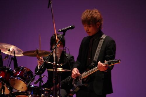スーツ姿でギター、ドラム演奏している二人の男性の写真