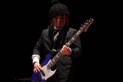 スーツ姿にニット帽でギターを演奏をしている男性の写真