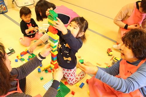 ブロックのおもちゃを積み上げて遊でいる子どもたちと保育ボランティアの方の写真