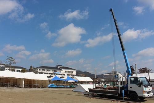 白と青色のテントが建ちクレーン車の停まった準備中の広場の写真