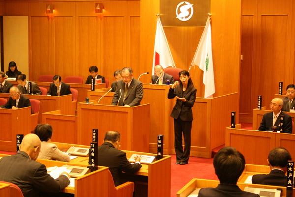 市議会演壇で一般質問をする議員の隣で手話通訳をする女性の写真