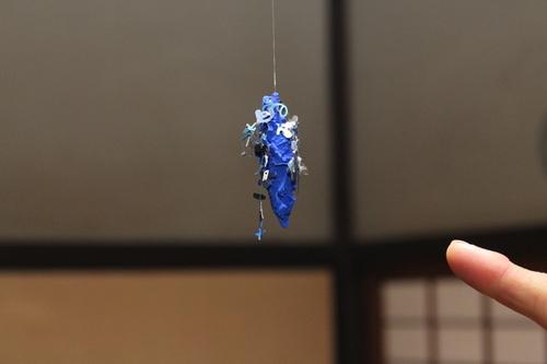 細かな装飾が付いた青色のみのむしが空中に吊るされている造形作品を指さしている写真