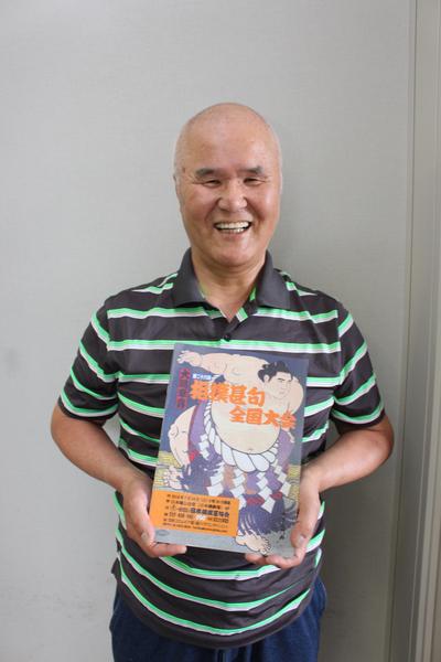 笑顔で相撲甚句全国大会と書かれた本を両手で持つ花井悟さんの写真