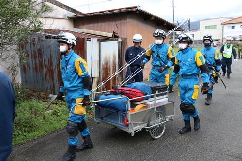 黄色と青の制服を身にまとった方々がリヤカーに資機材を載せ救助現場に向かっている様子の写真
