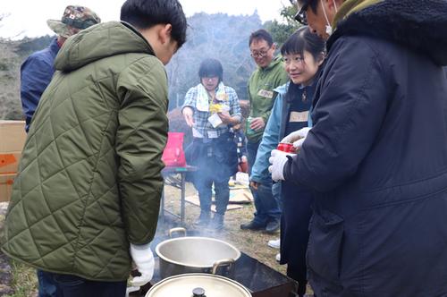 野外で湯気の上がる鍋を囲むピクニック参加者の写真