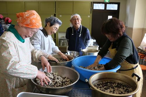 黒豆みそづくり講習会で黒豆と塩と麹を両手で混ぜ合わせている女性三人の写真