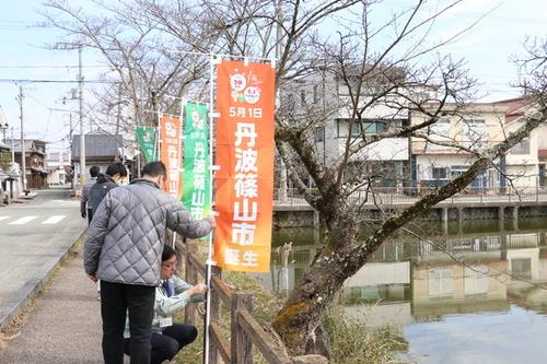 橋の手すりにのぼり旗「5月1日丹波篠山市誕生」をくくりつけている様子の写真