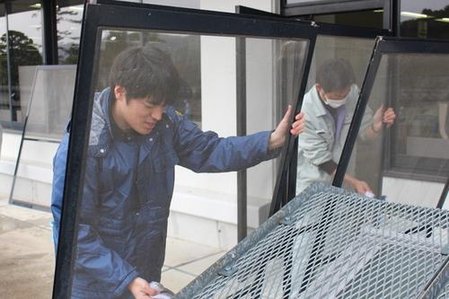 外された窓ガラスと金網を雑巾で綺麗に掃除している男性職員2人の写真