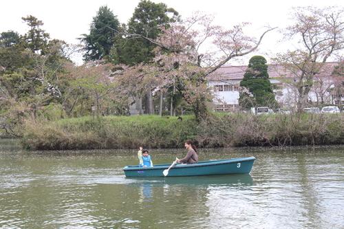 青色の観光ボートの上で右手を元気に上げている子供と笑顔でボートをこぐお母さんの写真