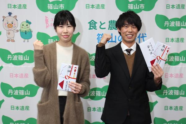 館山若潮マラソン激励のお祝いを持ちガッツポーズする雪岡誠太さんと足立幸子さんの写真