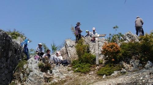 多紀連山頂上にて、ごつごつした岩に腰掛けてくつろぐ登山客の方々の写真