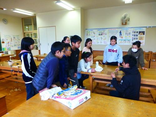 篠山産材をつかったお箸の作り方を教える小牧満也さんの手元を、熱心に見つめる子供たちの写真