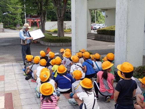 地面に座っている子供たちの前で、資料を手に黒塚先生がクイズを出している様子の写真