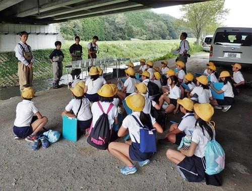 橋の下で篠山東雲高校の田井先生と生徒の皆さんのお話を座って聴く城南小学校の4年生の皆さんの写真