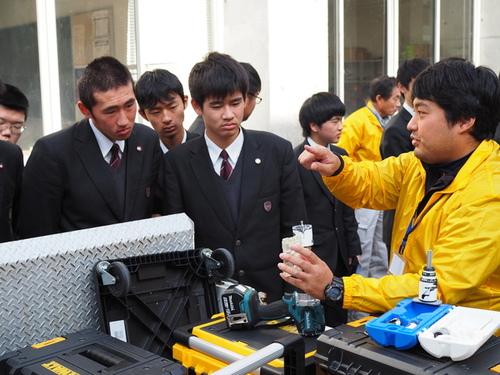 組合員が男子生徒たちへ電動インパクトレンチなどの作業工具を見せながら説明をする様子の写真