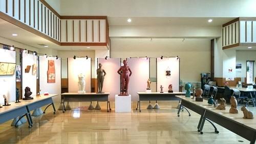 白い台座の上に展示されたえんじ色の裸体の彫刻作品と、周りに展示された人や動物がモチーフの個性豊かな彫刻作品の写真
