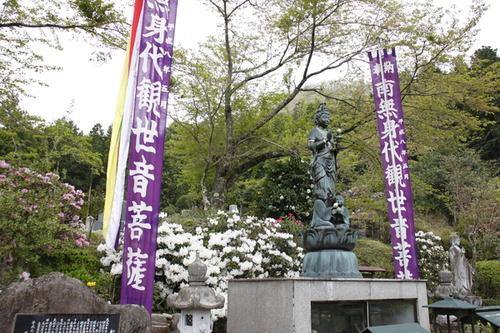 紫色の旗が左右にある銅像の後ろで、綺麗な白色のシャクナゲの花の写真