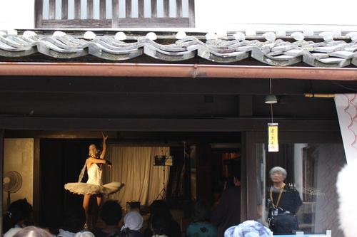 手前につられた風鈴がある町屋の中で白いチュチュを着た海外のアーティストがダンスを披露している様子の写真