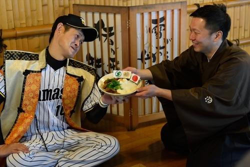 野球のユニフォームに陣羽織を着た男性と黒い和服を着た男性が篠山まるごと丼を一緒に持っている写真