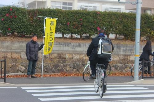 岡野小学校北交差点で自転車通学の学生にあいさつ運動する男性の写真