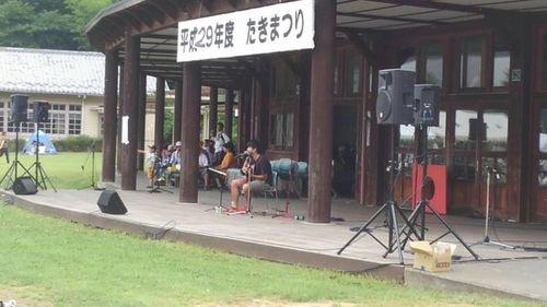 平成29年度 たきまつりと書かれた垂れ幕のかかるステージでの中森竜太さんによるギターの弾き語りの写真