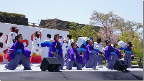 紫とオレンジの鮮やかな色の袴を着てステージ上で踊る男女の写真