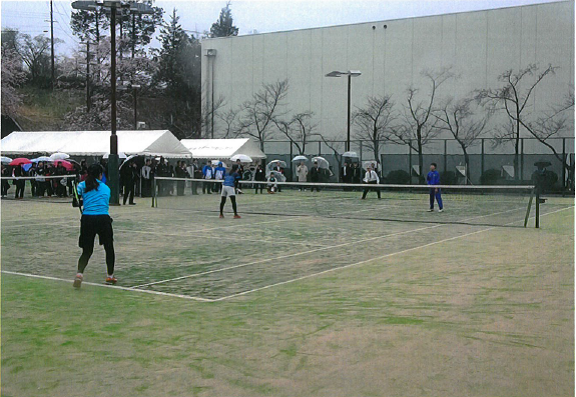 女性がボールを打ち、市長がテニスラケットでかまえている写真