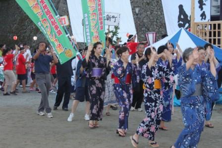 浴衣を着て踊っている人達の後ろを男性がデカンションと書かれたのぼり旗を持って歩いている写真