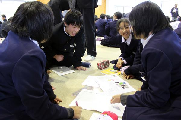 床に座る男女の生徒が、楽しそうに一緒にプリントを見ている写真